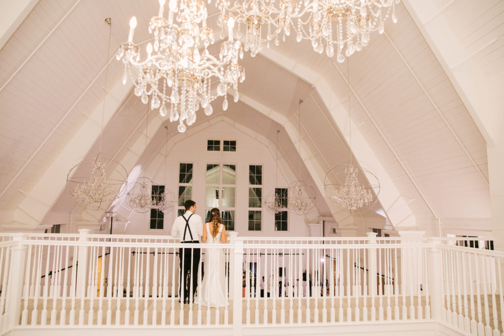 Bride and groom on balcony under chandeliers in white barn at wedding at Providence Vineyard Wedding Venue