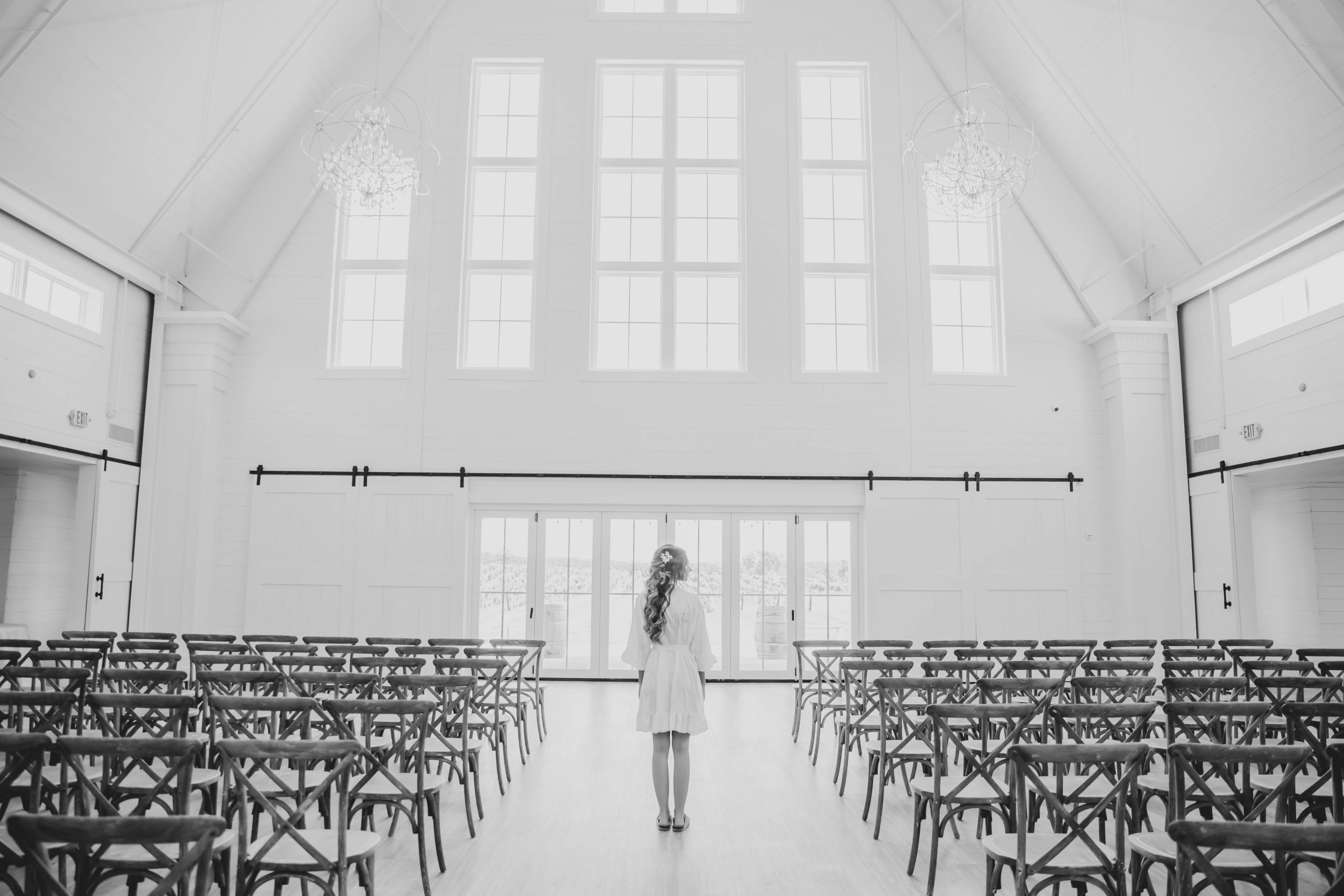 Bride looking out windows in white barn aisle at Providence Vineyard