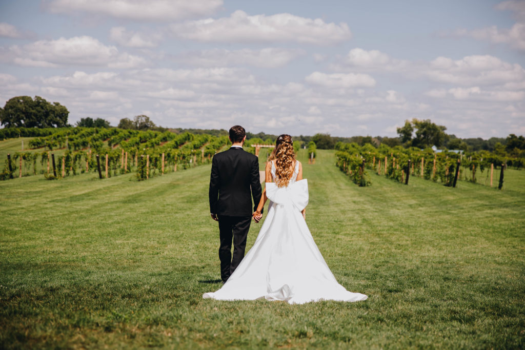 Bride and groom facing vineyard wearing white dress with large bow at Providence Vineyard
