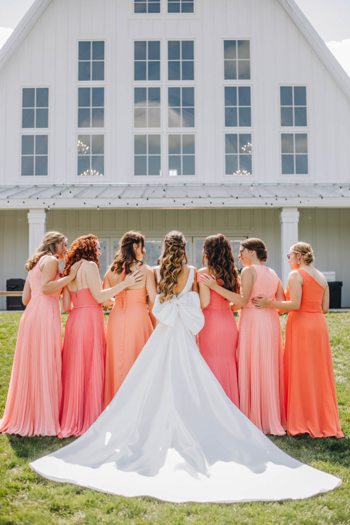 Bride and bridesmaids turned background bow dress in front of white barn at Providence Vineyard wedding venue