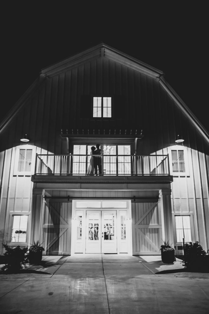 White barn at wedding at Providence Vineyard Wedding Venue at night bride and groom on balcony