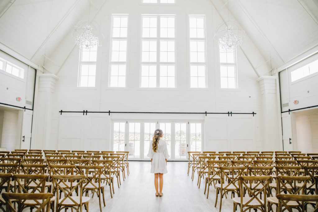 Bride looking at windows wedding ceremony in white barn with window backdrop at Providence Vineyard Wedding Venue